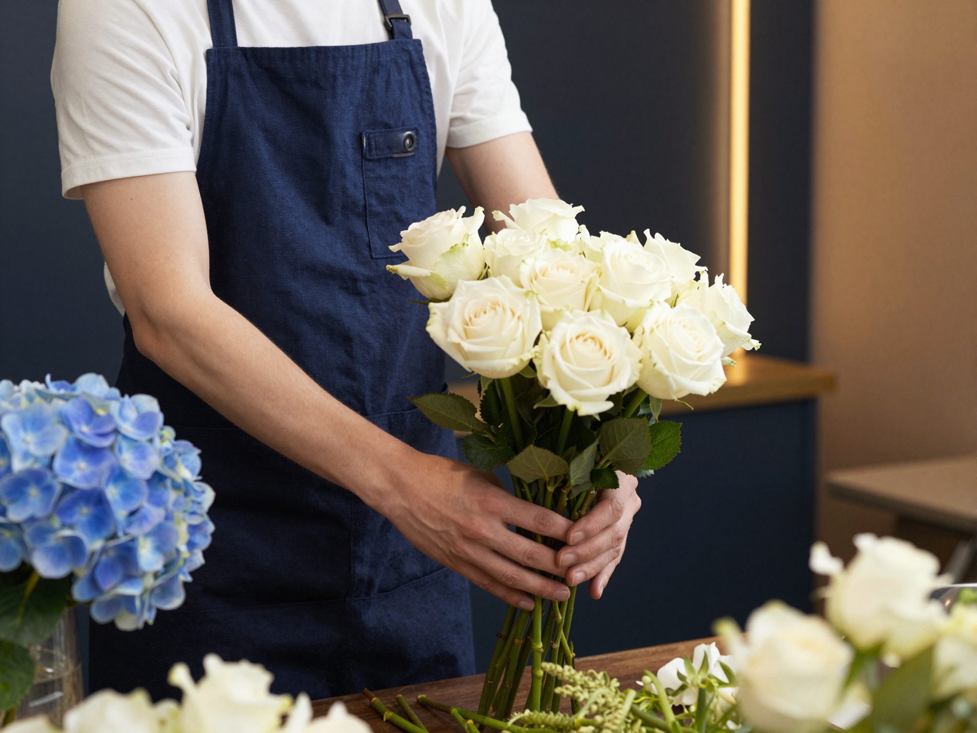 Fiorista Las Flores in grembiule navy compone rose bianche e ortensie blu